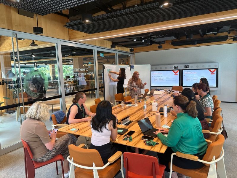Workshop in a modern office with facilitators at a whiteboard and screens showing reflection activity.
